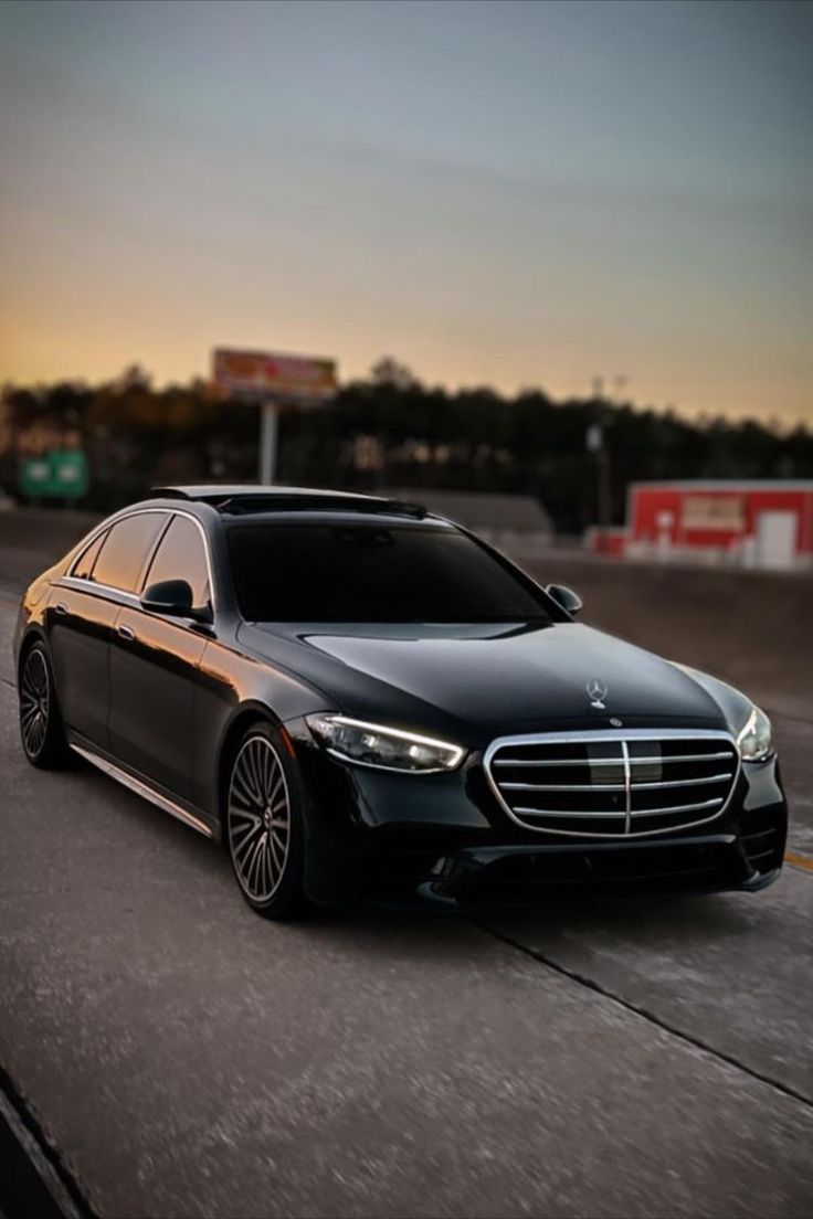 a black mercedes s - class is driving down the road at sunset or sunrise time