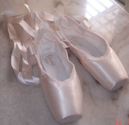 several pairs of white ballet shoes sitting on a counter top next to each other with ribbons around them