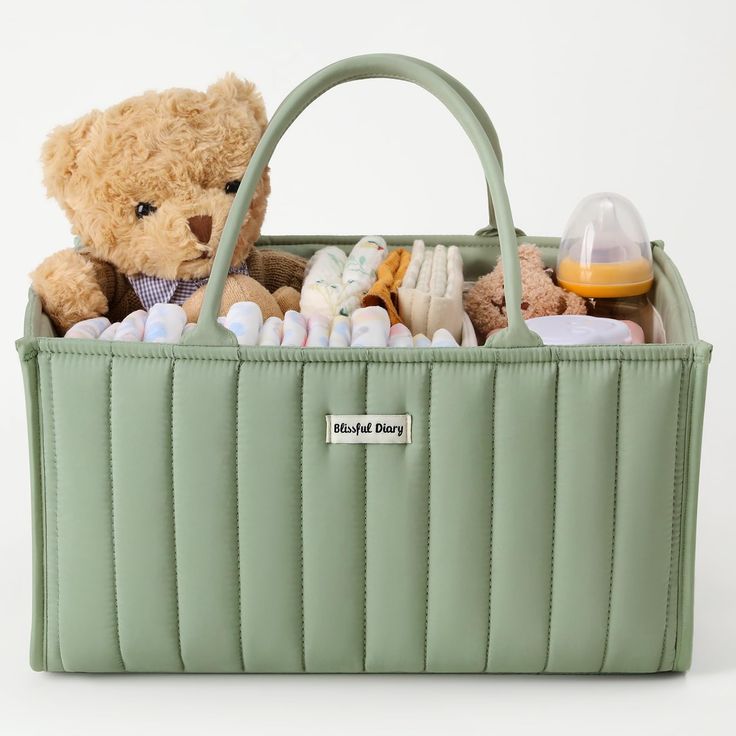 a teddy bear sitting in a green bag filled with baby items