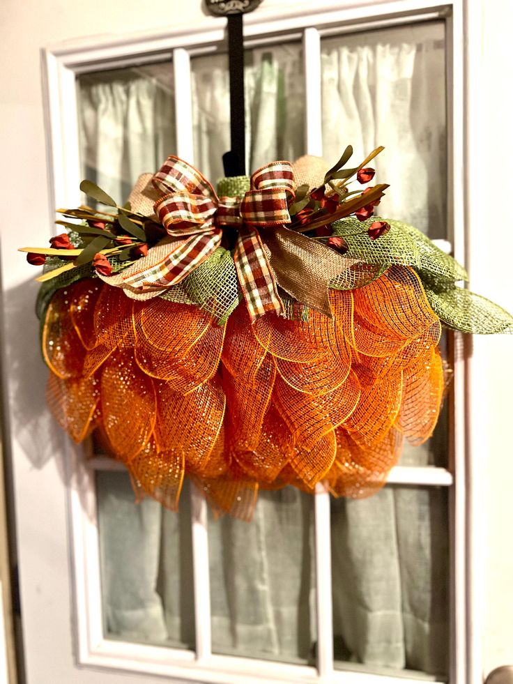 an orange mesh wreath hanging from the front door with leaves and berries attached to it