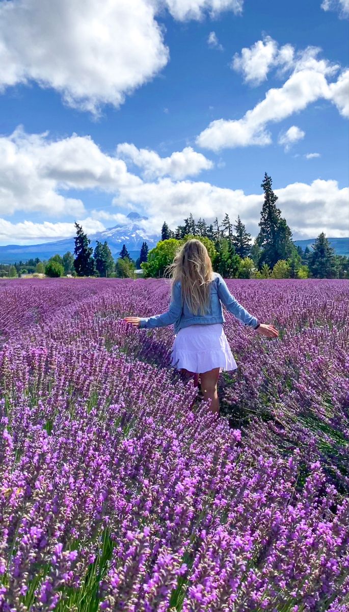 a girl walking through a field of lavender flowers