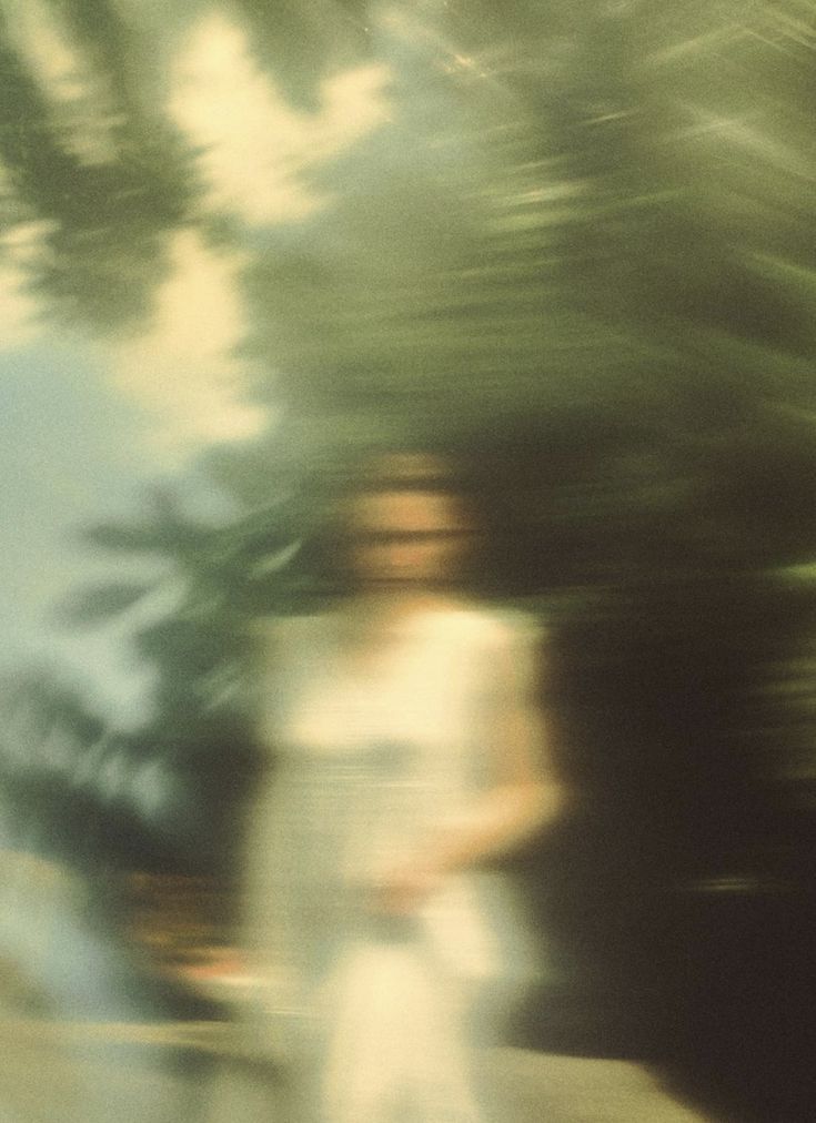 a blurry photo of a man riding a skateboard down a street with trees in the background