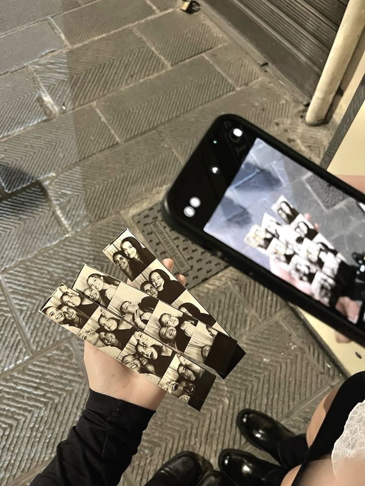 a person holding up some pictures in front of a cell phone on the ground,