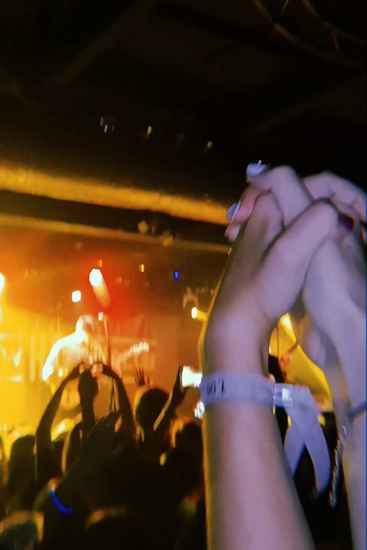 a person holding their hand up in front of a crowd at a concert with lights on