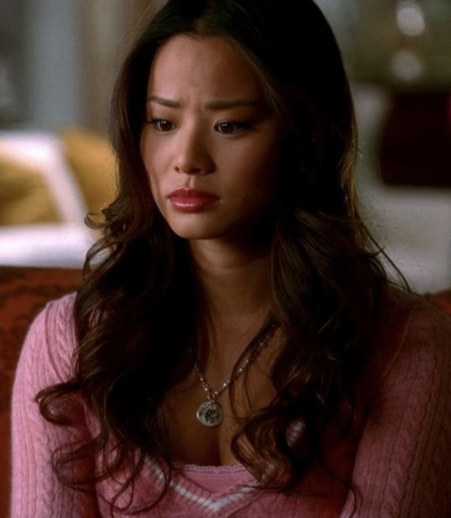 a woman sitting on top of a couch wearing a pink sweater and necklace in front of her face