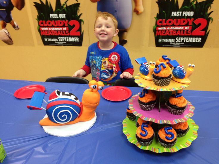 a young boy sitting at a table with cupcakes in the shape of animals