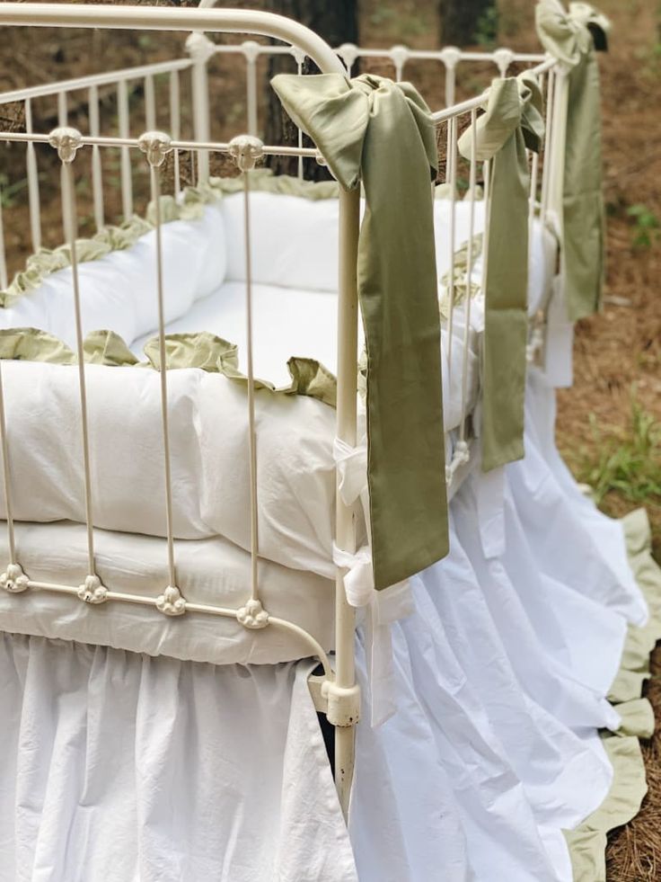 an old crib with white sheets and green bows on the top, sitting in some grass