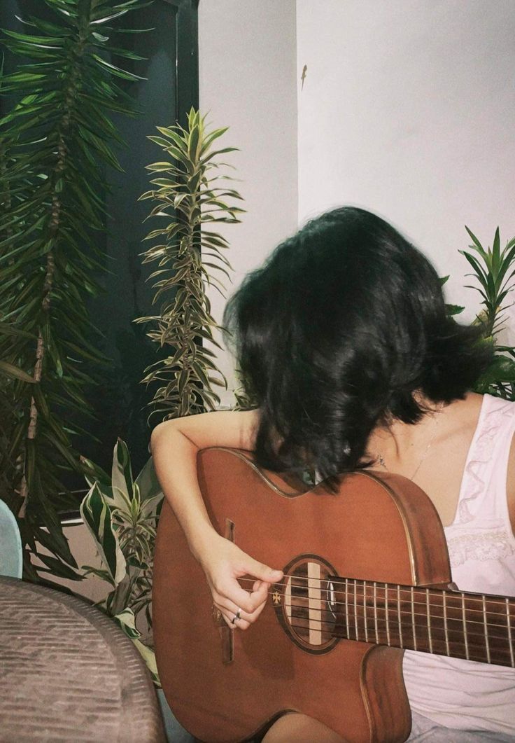 a woman is playing an acoustic guitar in front of a potted plant on the floor