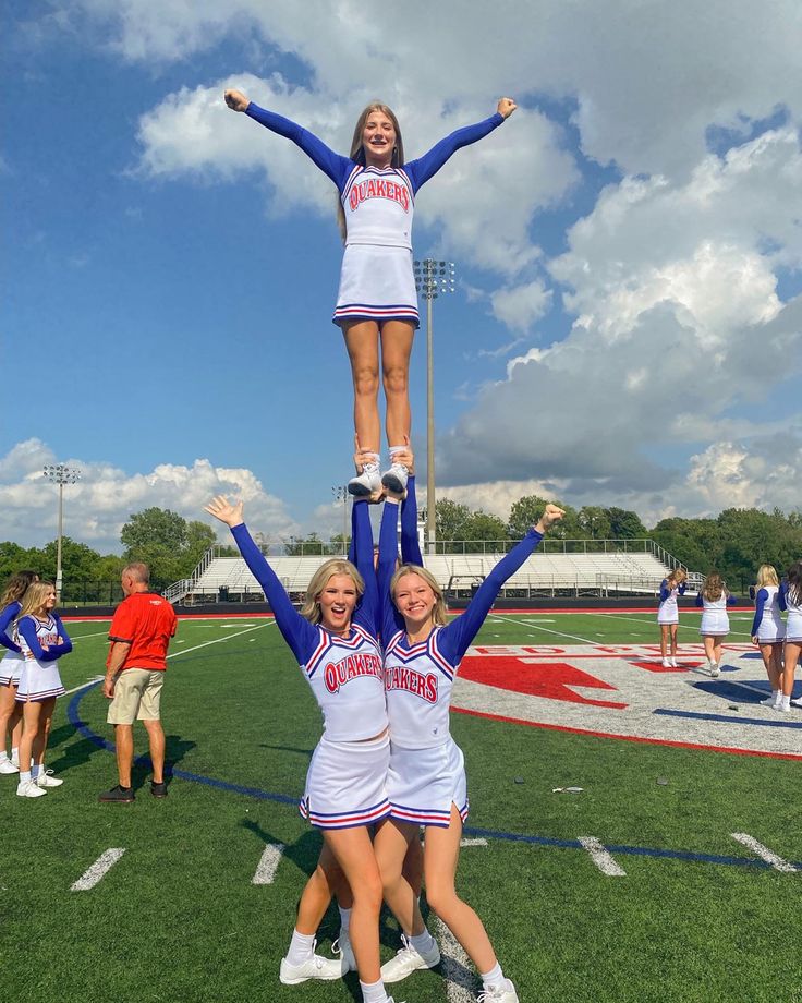 two cheerleaders standing on the back of each other while holding their hands in the air