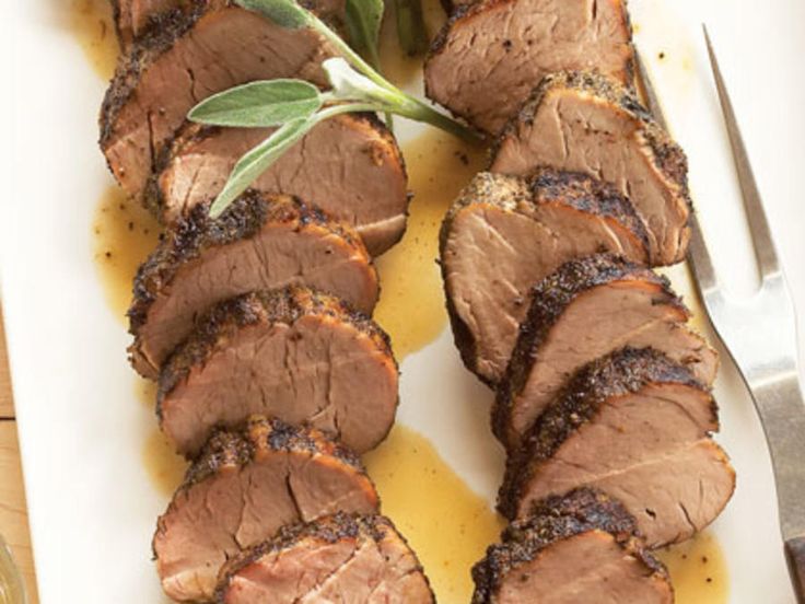 sliced meat on a white plate next to a knife and fork with green sprigs