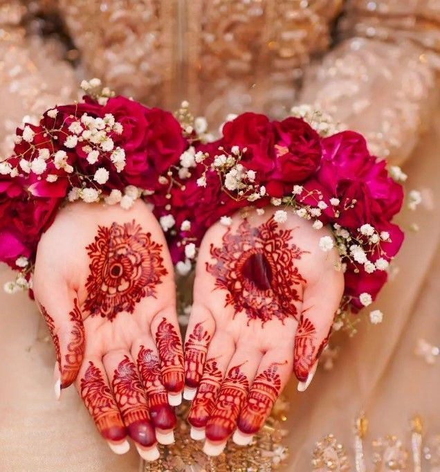 two hands with hendi and flowers on their palms in front of the bride's face