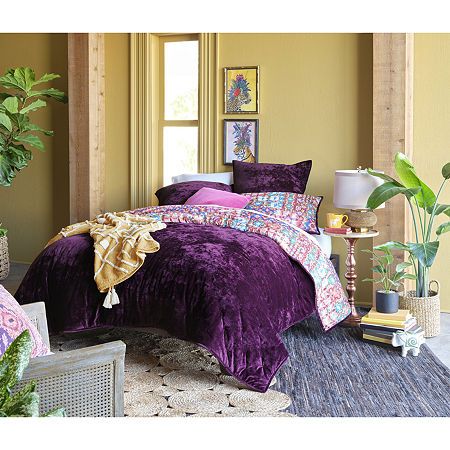 a bedroom with yellow walls and purple bedding in the corner, potted plant next to it