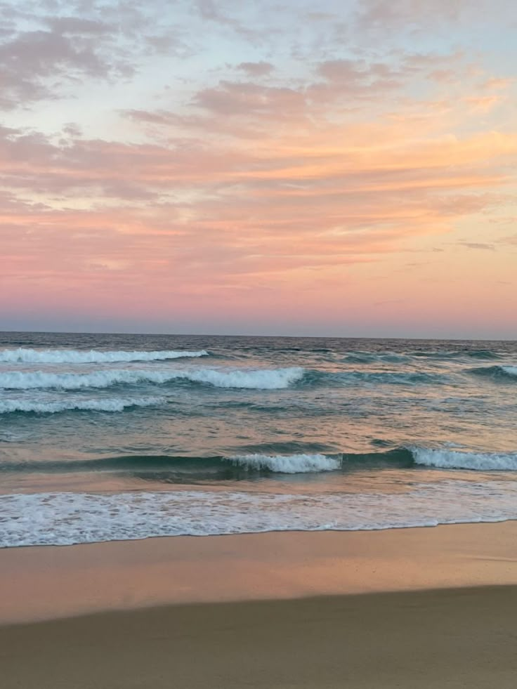 an ocean beach with waves coming in to shore and the sun setting on the horizon