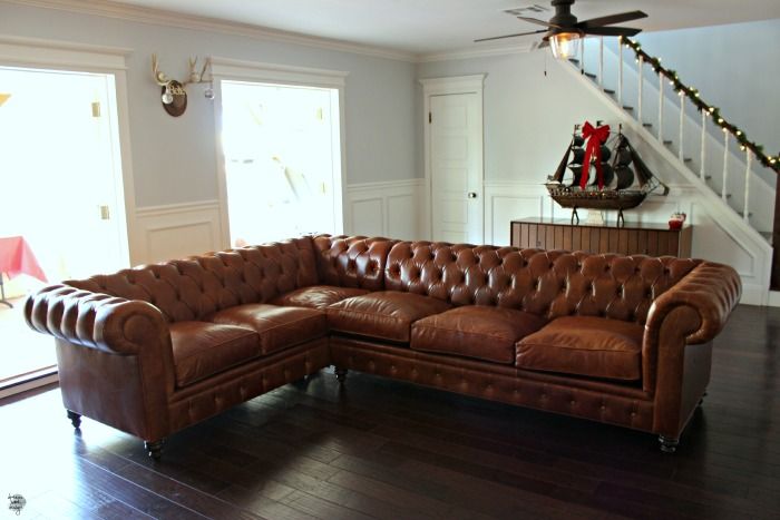 a large brown leather couch sitting in a living room next to a stair case and window