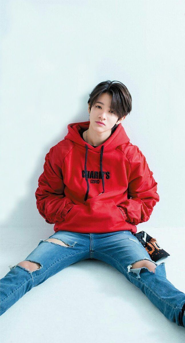 a young man sitting on the floor wearing a red hoodie and ripped blue jeans