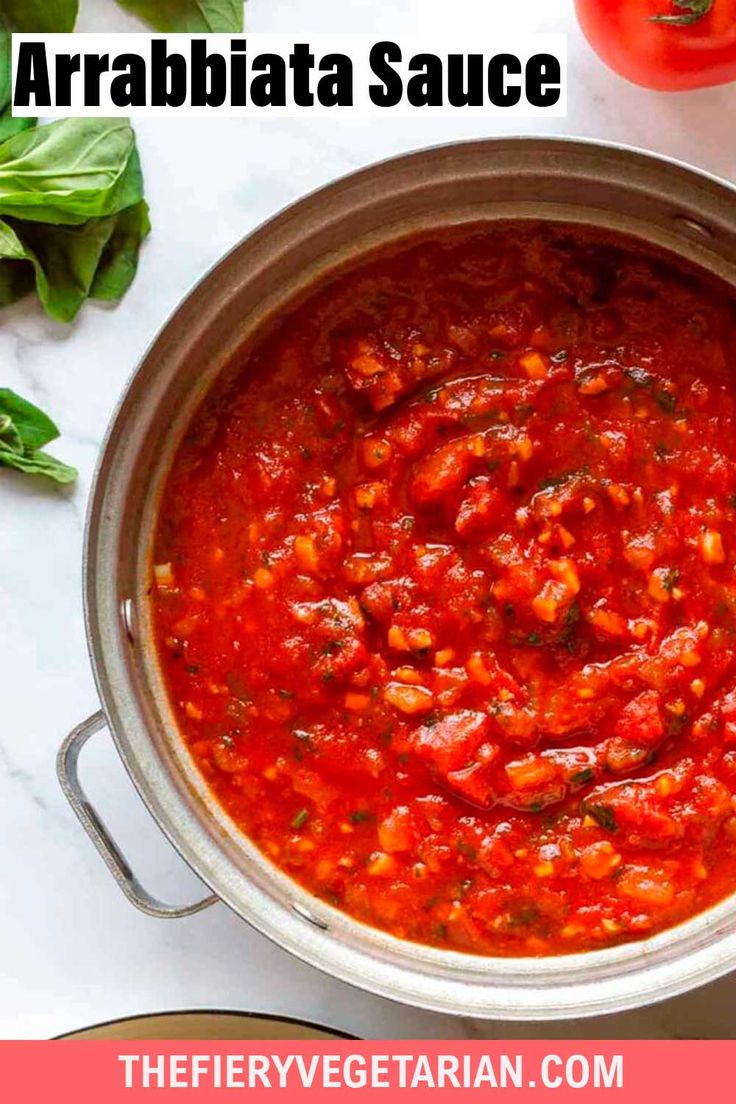 a pot filled with tomato sauce next to fresh basil leaves and tomatoes on the side