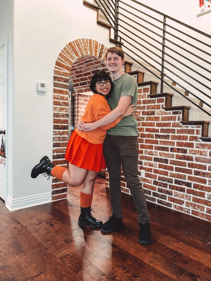 a man and woman posing for a photo in front of a brick wall, with their arms around each other