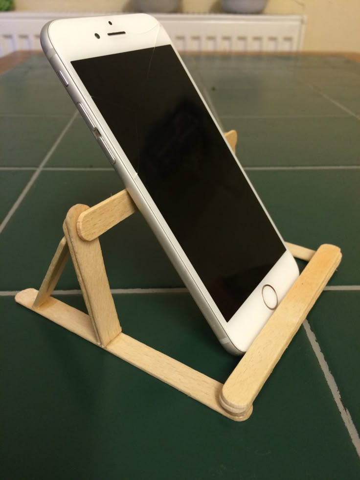 an iphone is sitting in a wooden stand on the floor next to a potted plant