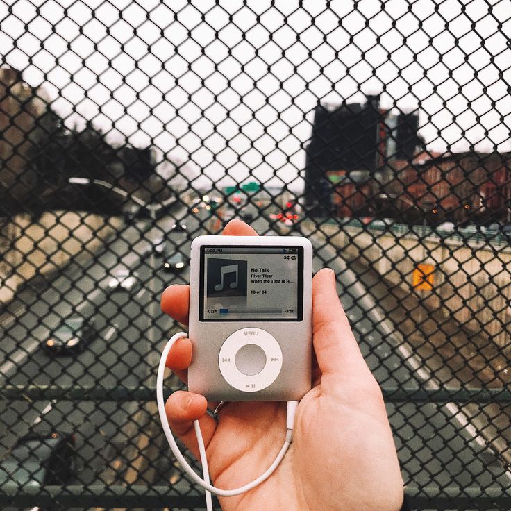 a hand holding an ipod in front of a fence