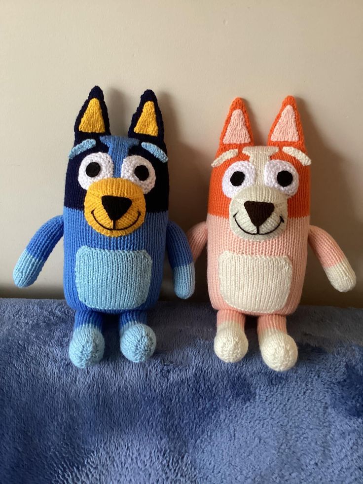 two knitted stuffed animals sitting next to each other on a blue blanket in front of a wall