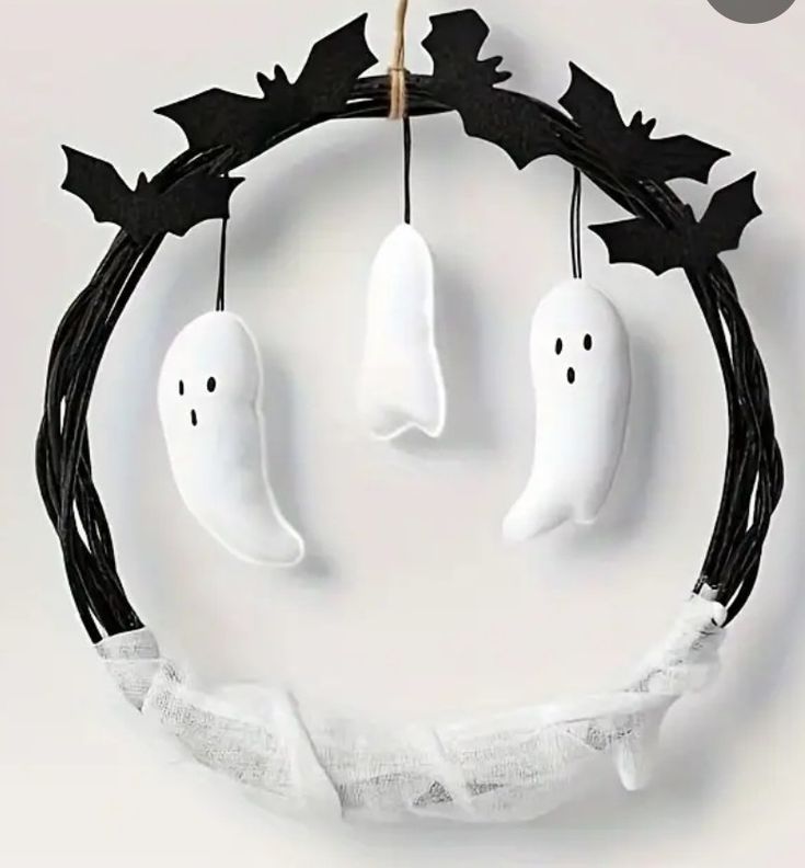 two white ghost heads hanging from a black wreath with bats and leaves on it's sides