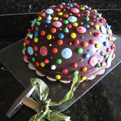 a chocolate cake decorated with colorful candies on top of a black table next to a knife