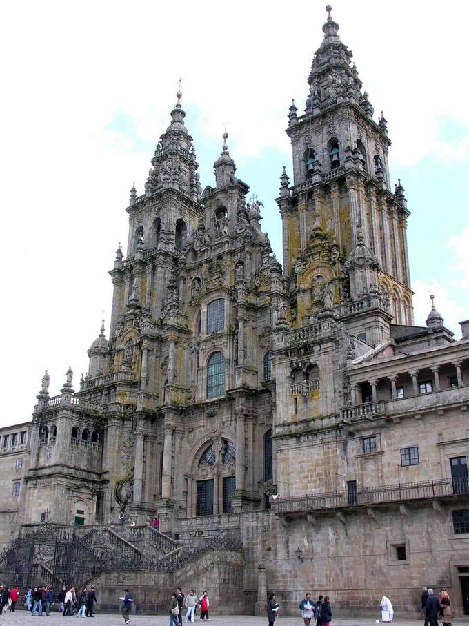 people are walking around in front of an old building with many towers and spires