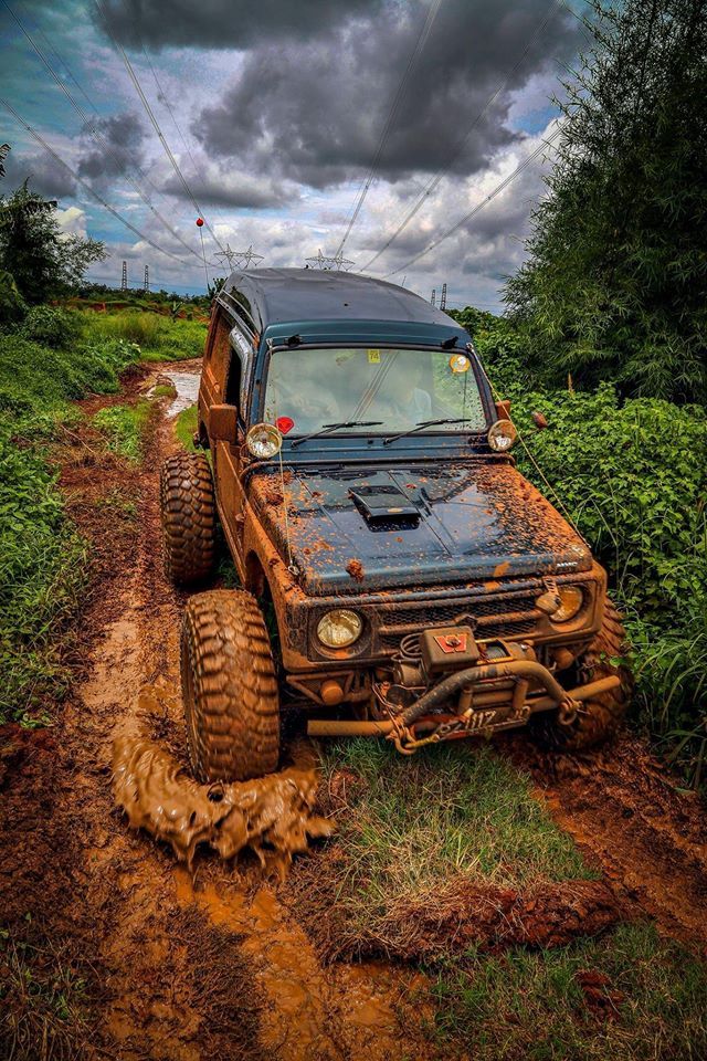 an old truck is stuck in mud on the side of a dirt road with clouds overhead