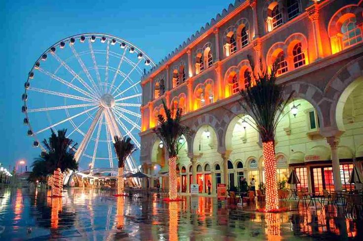 a large ferris wheel sitting next to a building with lights on it's sides