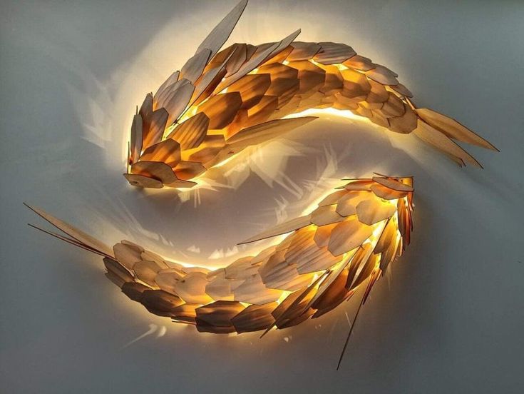 an artistic sculpture made out of paper with lights on the sides and feathers attached to it