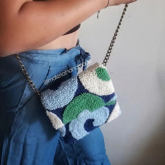 a woman is holding a purse made out of crocheted material with chains attached to it