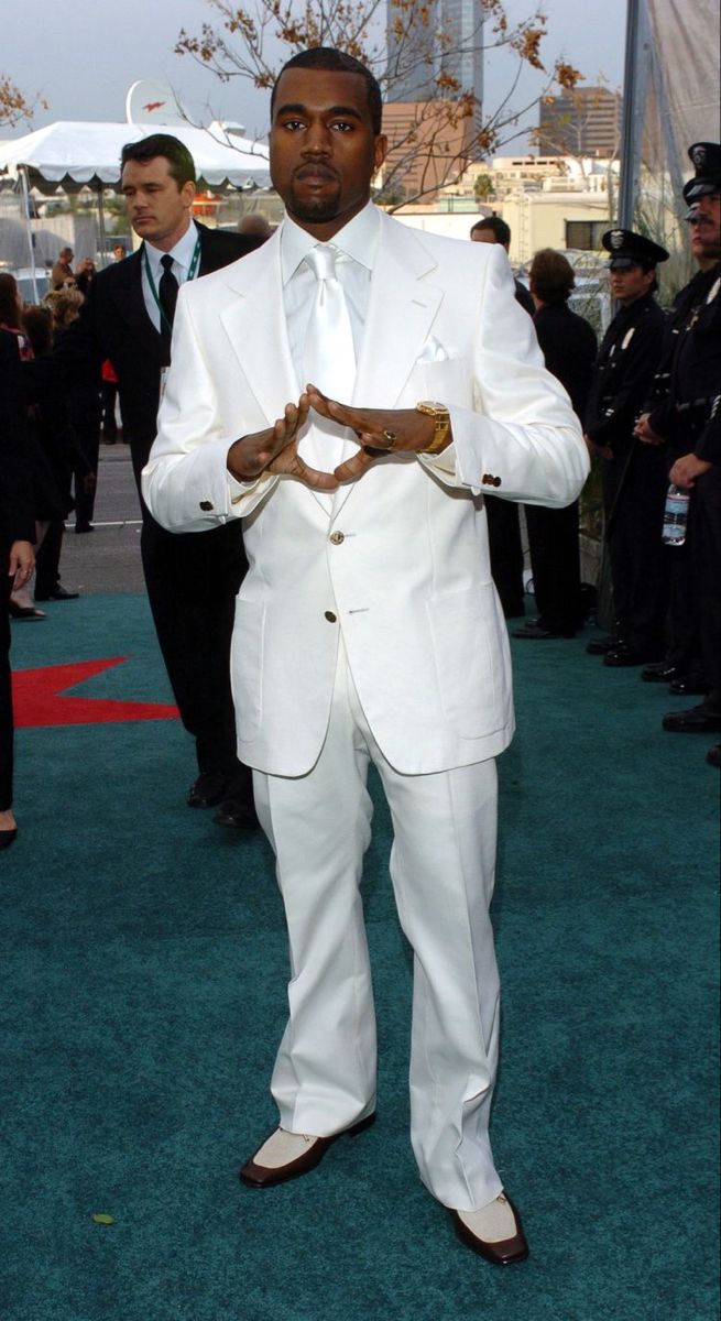 a man in a white suit and tie standing on the green carpet at an event