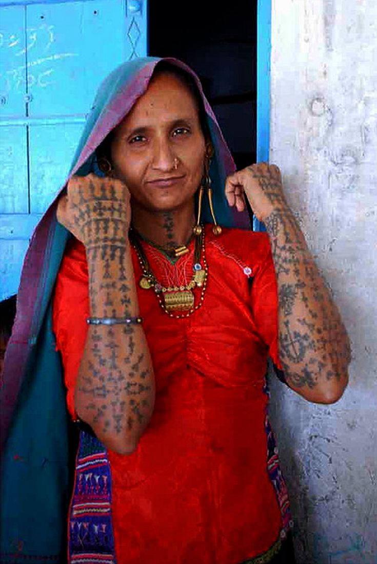 a woman with tattoos on her arms and chest standing in front of a blue door