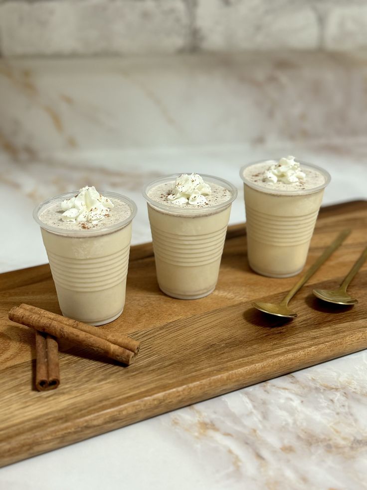 three cups with whipped cream and cinnamon on a wooden tray