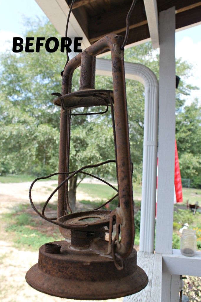 an old rusted light hanging from the side of a house with trees in the background