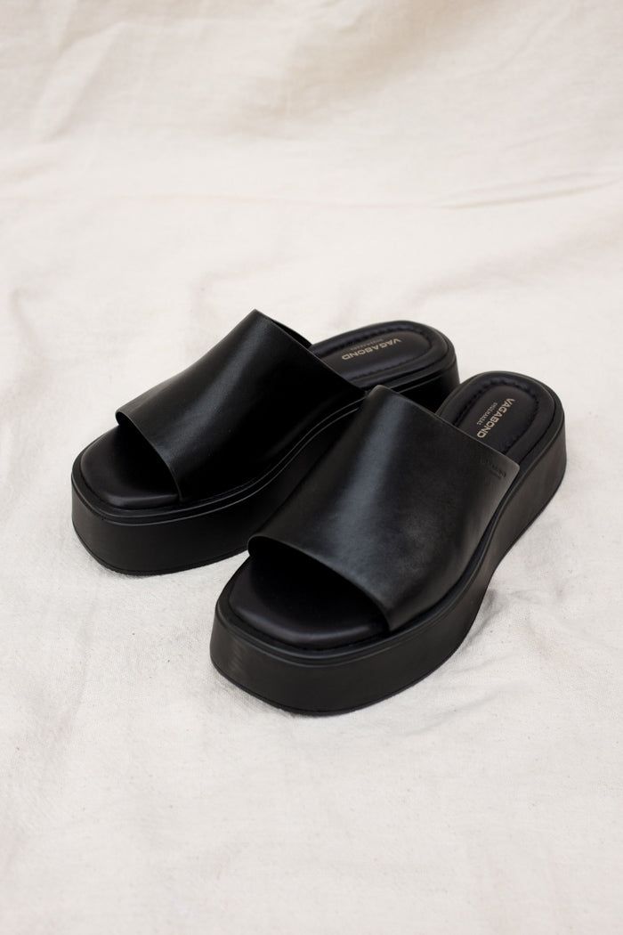 Vagabond Shoemakers Courtney platform slides. It is all about the characteristic flared outsole that makes this pool slide style the ultimate sandal of the season. The simple slip-on upper, made from black leather, is grounded by tonal flatform soles measuring 50 mm. Details include padded insoles and square toes. 5134-001-92 5334-601-92 Flatforms Sandals, Black Slip On Sandals, Black Slide Sandals, Black Sandals Platform, Platform Slide Sandals, Slide On Shoes, Slippers Summer, Black Platform Slides Outfit, Shoes Slides