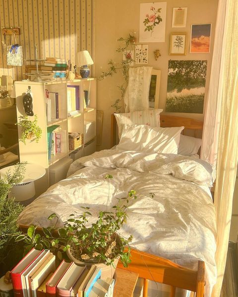 an unmade bed in a bedroom with books on the floor and pictures above it