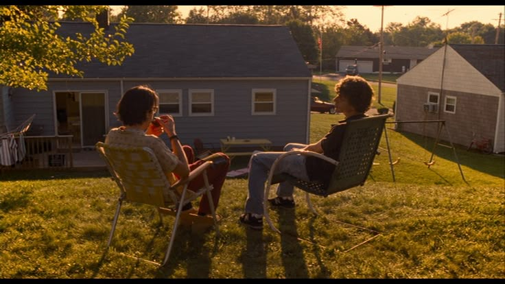 two women sitting in lawn chairs talking to each other on the grass near a house