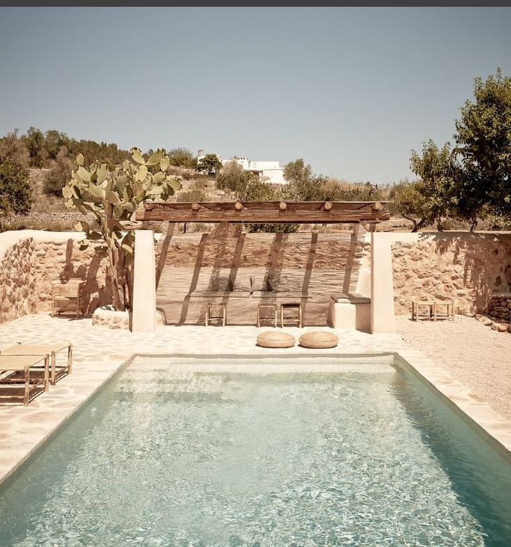 an outdoor swimming pool surrounded by stone walls and cactus trees in the background, with two lounge chairs next to it