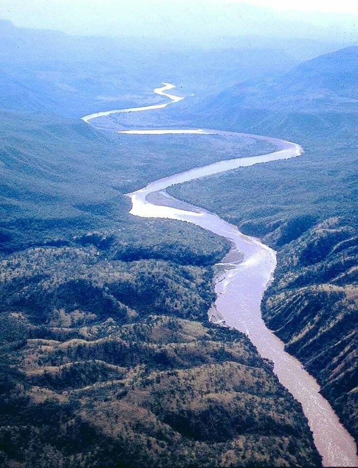 an aerial view of a river in the middle of some hills and valleys with trees on both sides