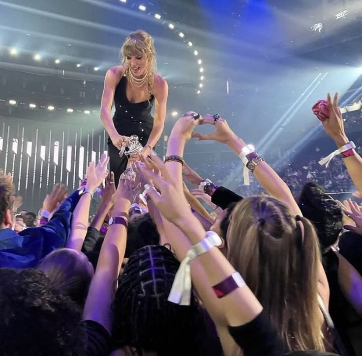 a woman in black dress standing on top of a stage surrounded by people holding their hands up