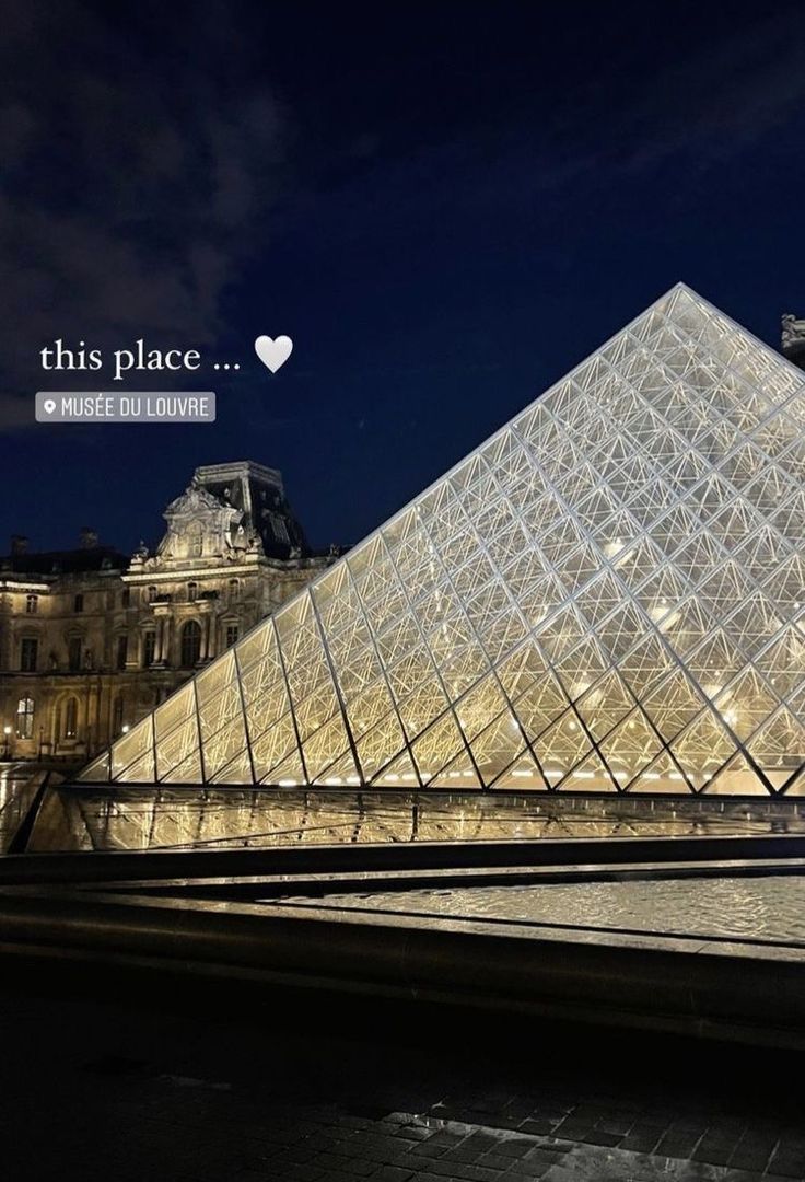 the pyramid is lit up at night in front of a building with a large glass window