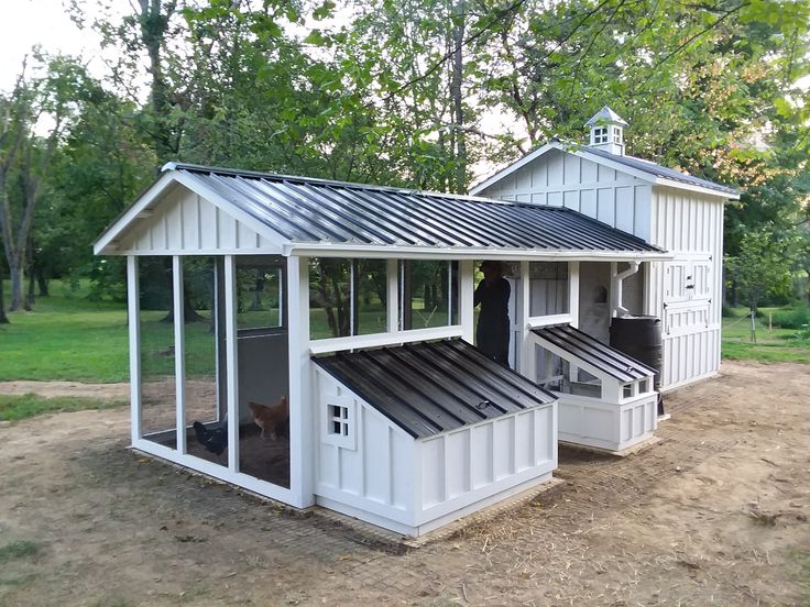 a small white chicken coop in the middle of a field with trees and grass behind it