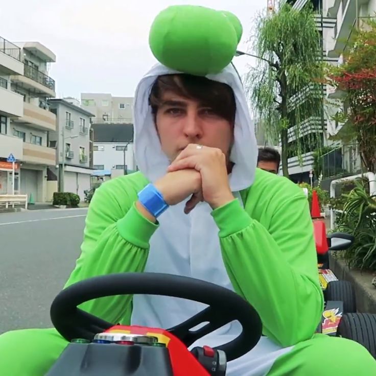 a man in a green costume is sitting on a toy car and looking at the camera