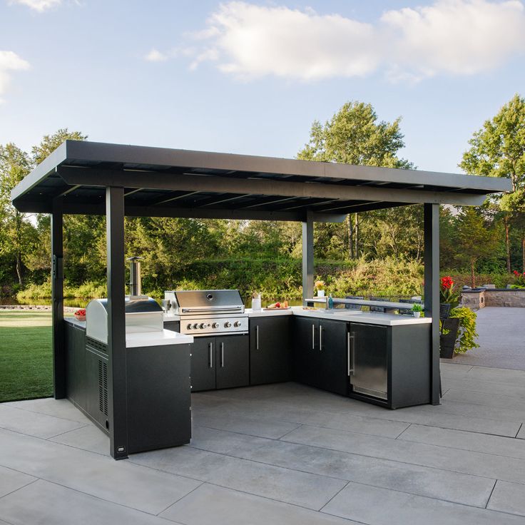 an outdoor kitchen with grills and sink in the middle of a patio area next to a grassy field