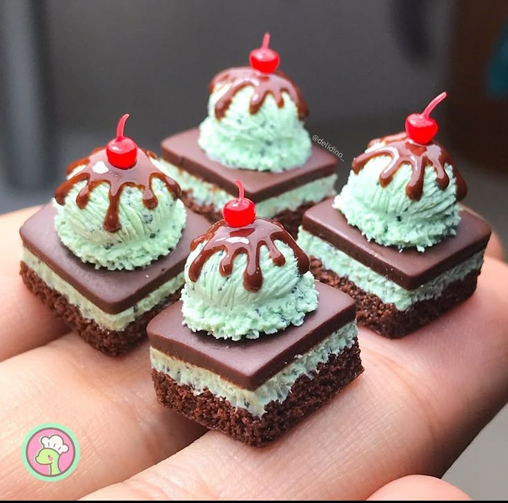 four pieces of cake sitting on top of each other in someone's hand with chocolate frosting and cherries