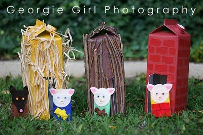 three small figurines sitting in the grass next to a red brick house and black cat