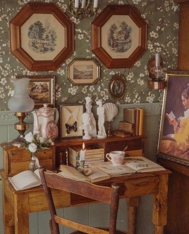 an old fashioned desk with two pictures on the wall and candles in front of it