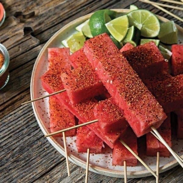 several skewers of watermelon on a plate with limes and other ingredients