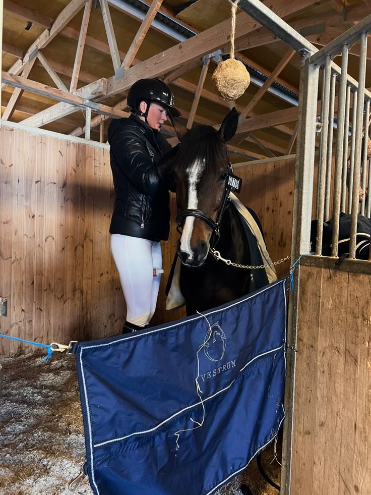 a woman in riding gear standing next to a brown and white horse with a blue flag